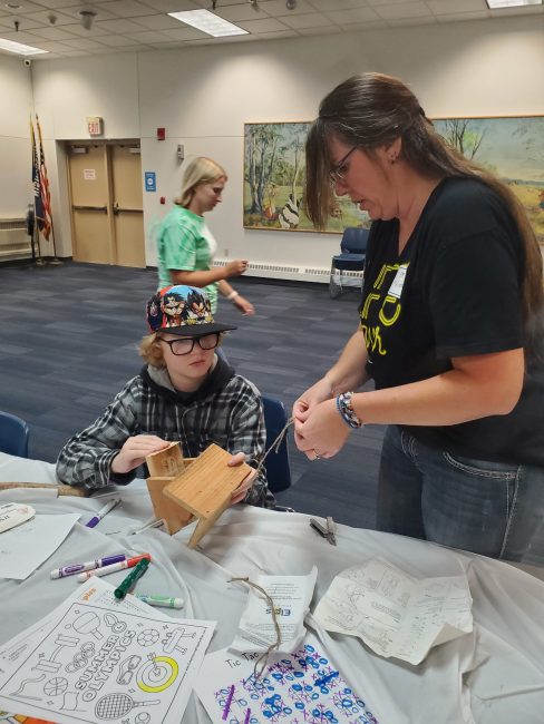 A boy and woman working on assembling a bird house together. 